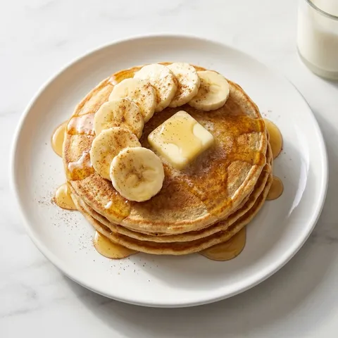 Stack of banana oat pancakes with honey drizzle and banana slices on a plate