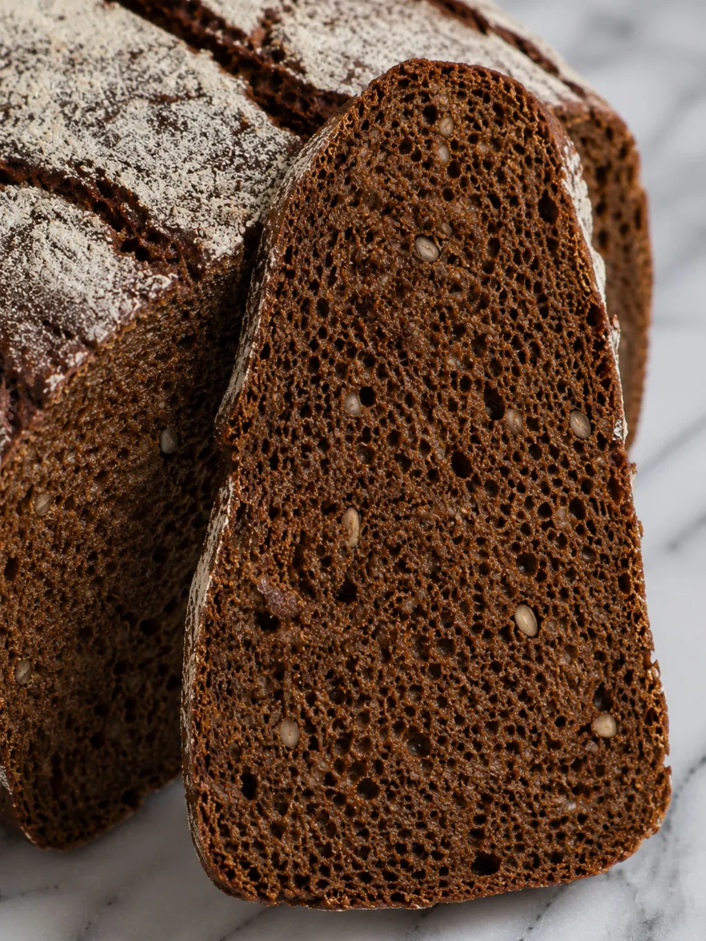 Thick slice of dark rye sourdough bread with caraway seeds standing against the loaf
