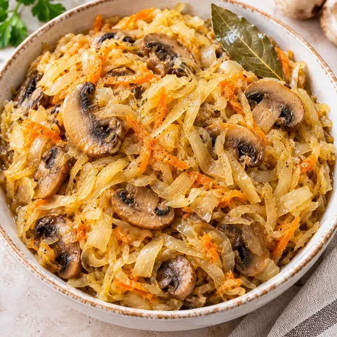 Kapusta z pieczarkami w jasnej misce z widoczną marchewką i cebulą