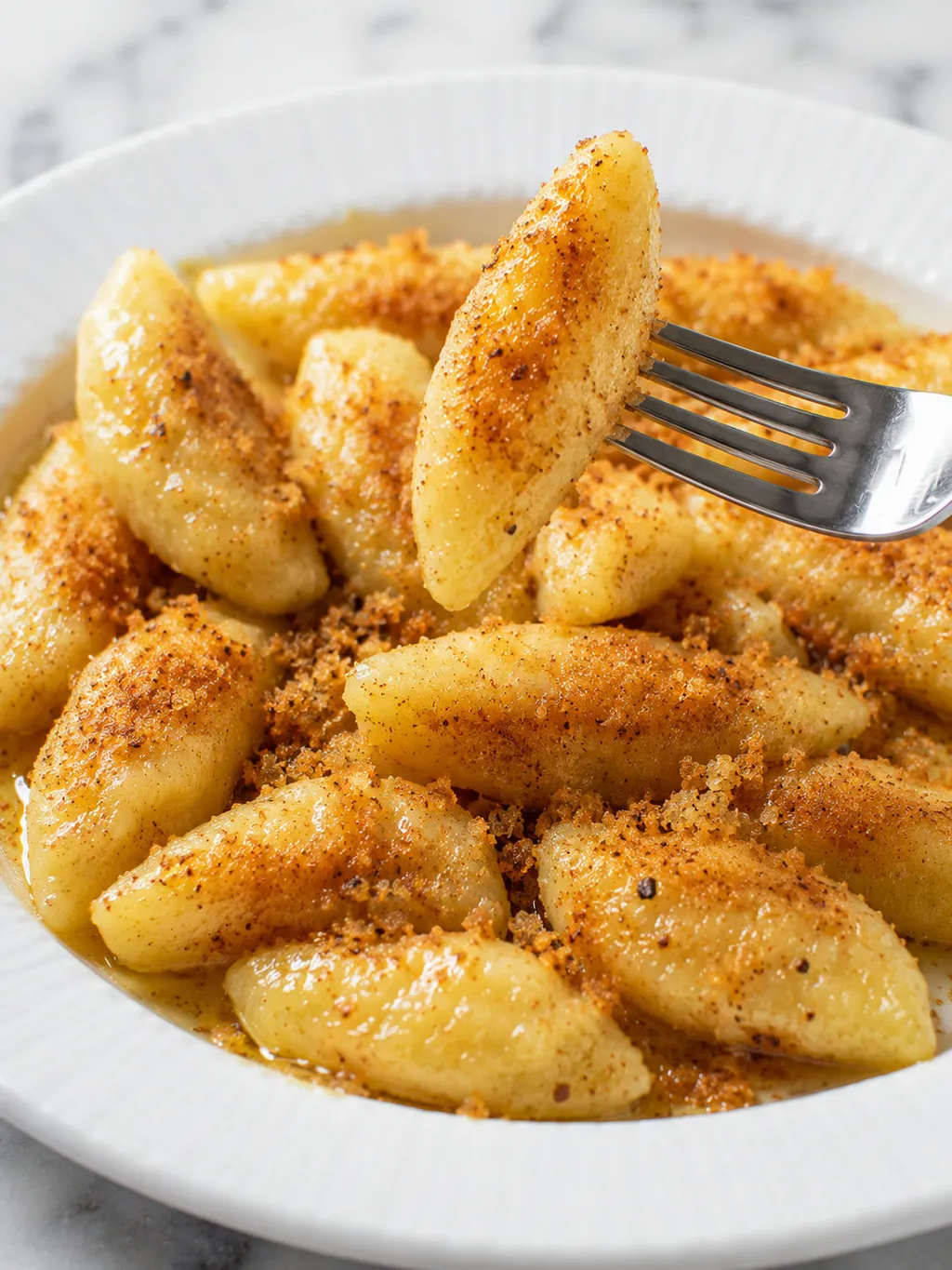 Close-up of buttery Polish kopytka potato dumplings with toasted breadcrumbs on a fork