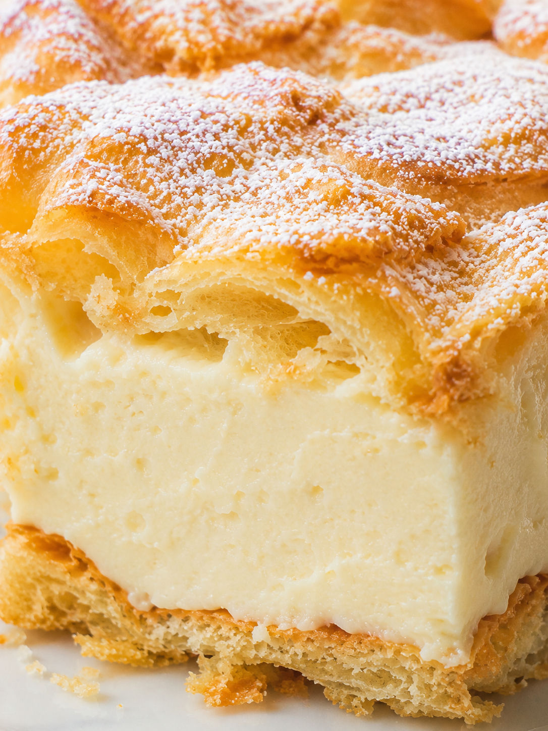 Tall slice of healthier karpatka with vanilla cream and powdered sugar