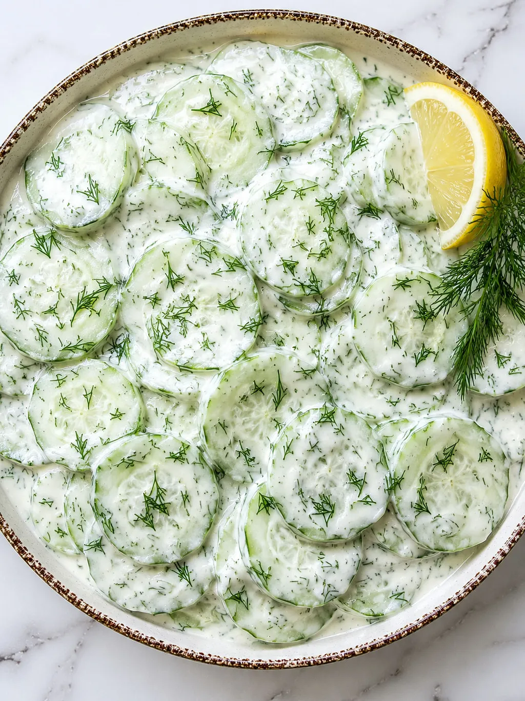 Top-down bowl of creamy cucumber salad with sour cream and fresh dill
