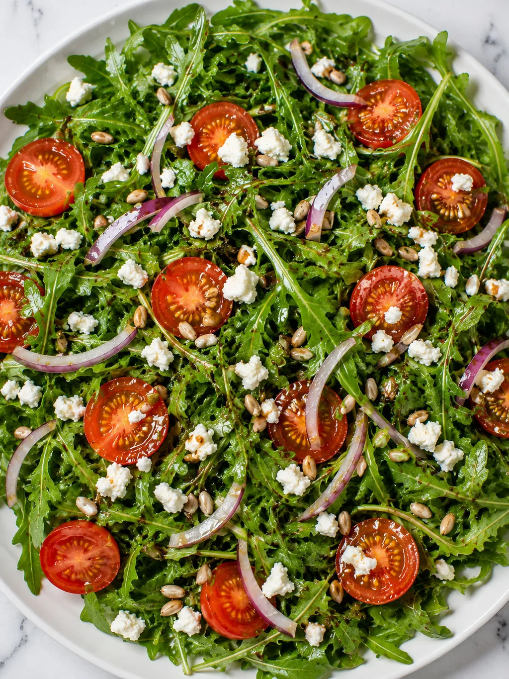 Top-down view of arugula salad with cherry tomatoes, feta and red onion