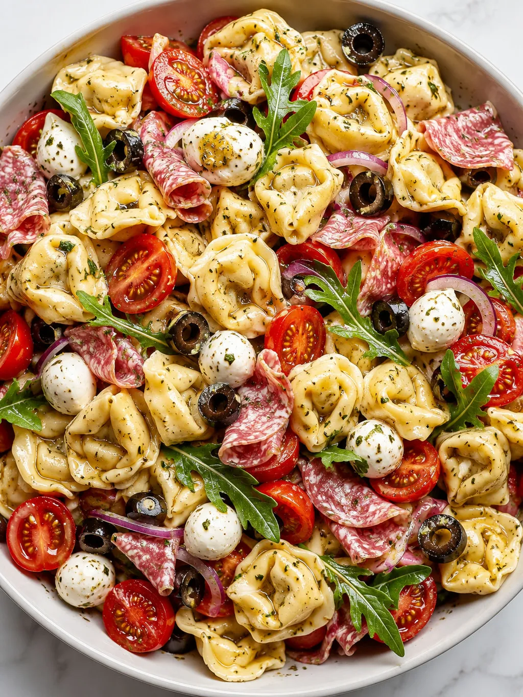 Top-down bowl of tortellini salad with tomatoes, mozzarella and salami